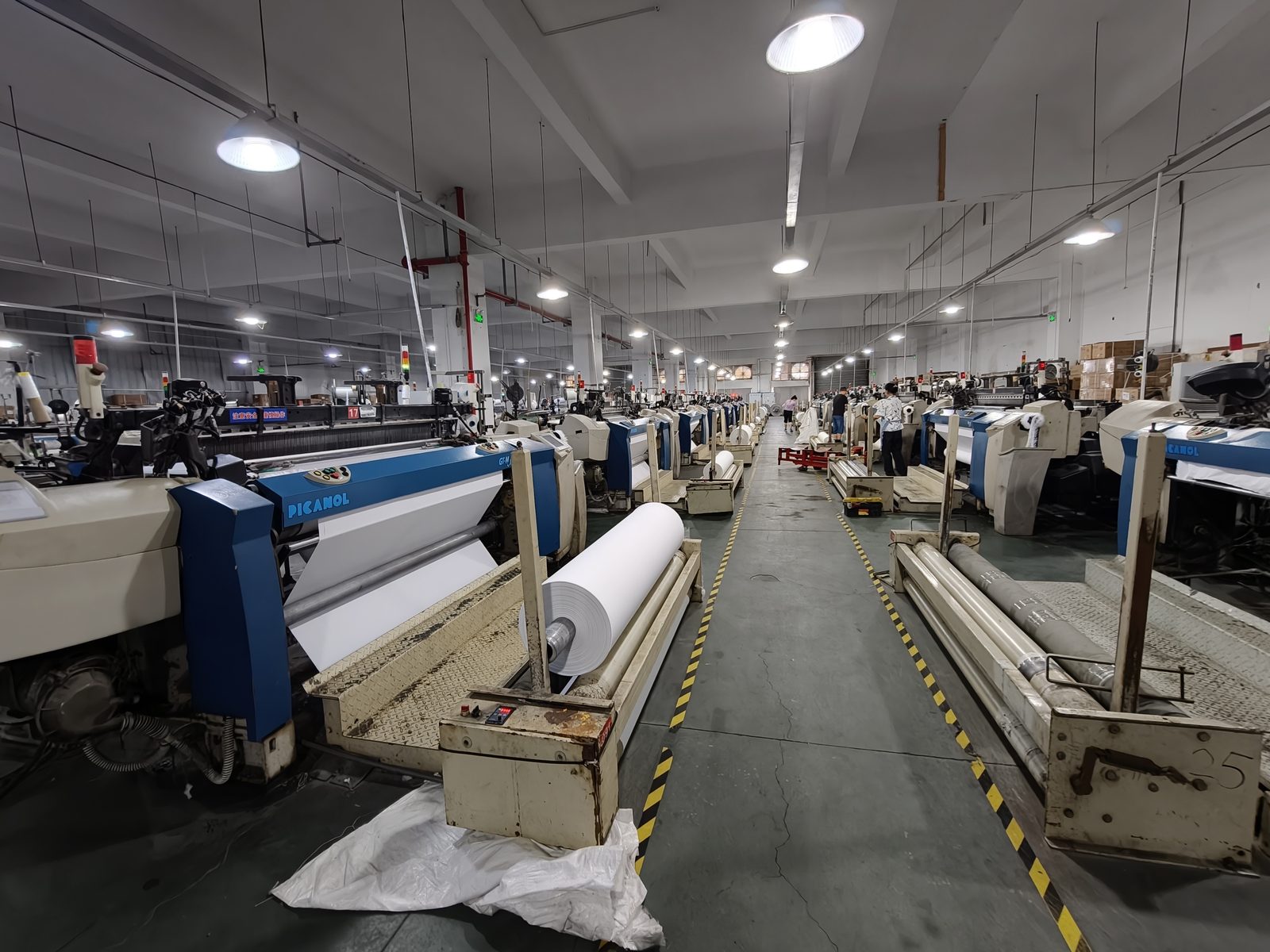 Air-jet weaving hall with rows of looms and greige fabric rolls at Yongbo Textile mill, Jiaxing